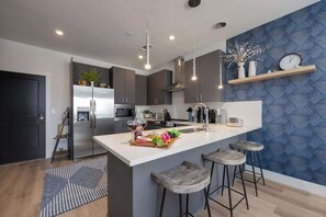 Una cocina moderna con una isla central, taburetes de bar y un papel tapiz azul con estampado.