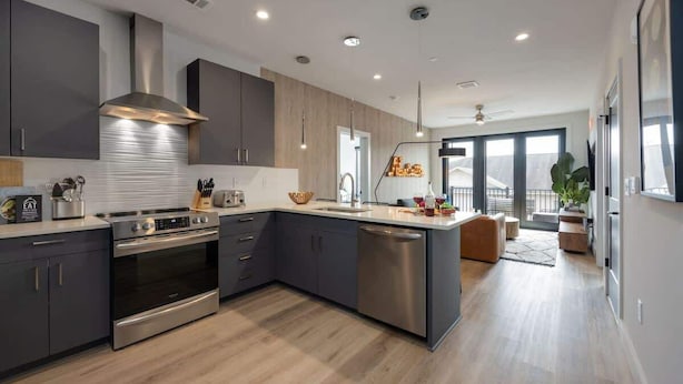 Une cuisine moderne avec des meubles de couleur sombre, des appareils électroménagers en acier inoxydable et un grand îlot central.