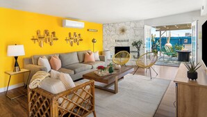 A living room with a yellow wall, a stone fireplace, and a view of the outdoor patio. - Pool + Spa + Stargazing: Stylish Mid-Century Home Near Joshua Tree National Park (Twentynine Palms)
