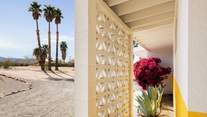 A building with a beige lattice fence, a palm tree, and a pink flower. - Pool + Spa + Stargazing: Stylish Mid-Century Home Near Joshua Tree National Park (Twentynine Palms)