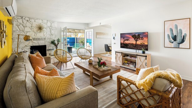 A living room with a stone fireplace, a sofa, a coffee table, and a television. - Pool + Spa + Stargazing: Stylish Mid-Century Home Near Joshua Tree National Park (Twentynine Palms)