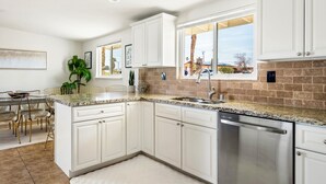 A modern kitchen with white cabinets, granite countertops, and a stainless steel dishwasher. - Pool + Spa + Stargazing: Stylish Mid-Century Home Near Joshua Tree National Park (Twentynine Palms)