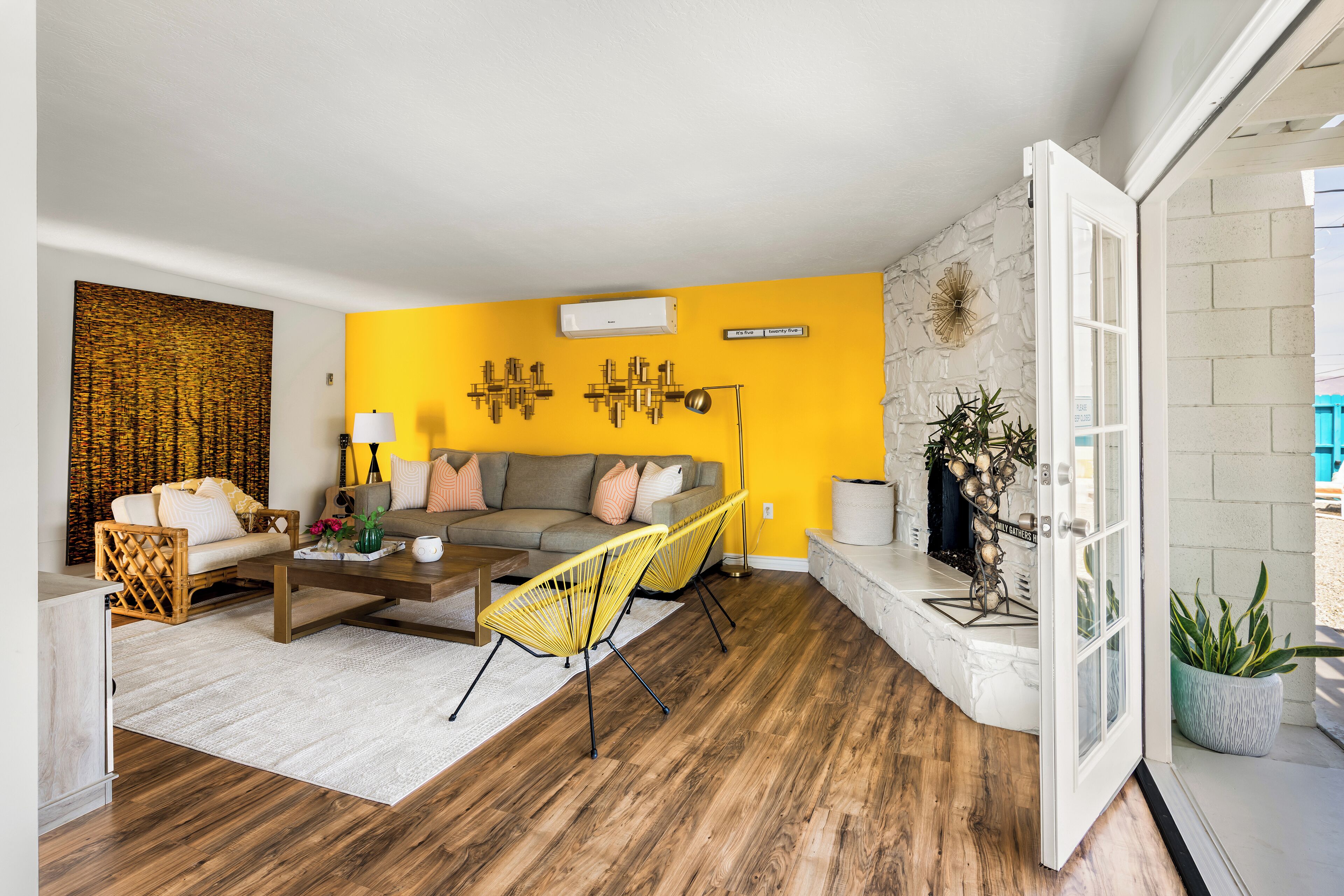 Een woonkamer met een gele wand, een bank, een salontafel en twee gele stoelen.