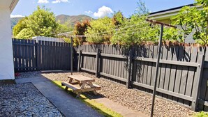A backyard with a wooden fence, a picnic table, and a garden area. - Comfortable stay for 6 / Perfect for family trip (Lower Hutt)