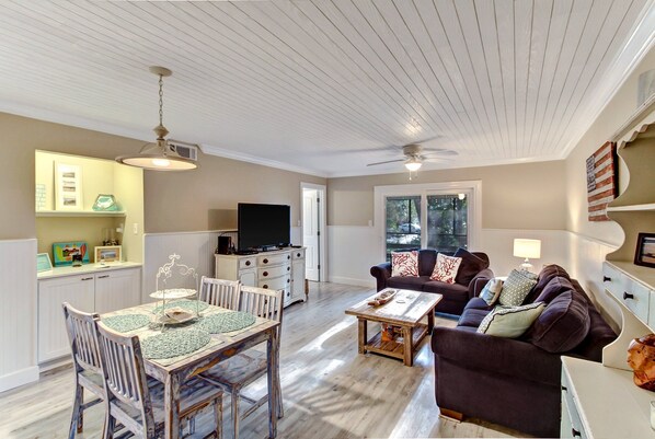 A spacious living area with a dining table, a sofa, and a TV in the background. - Walk to Beach, Super Large Screened Patio - Amelia Island (Fernandina Beach)