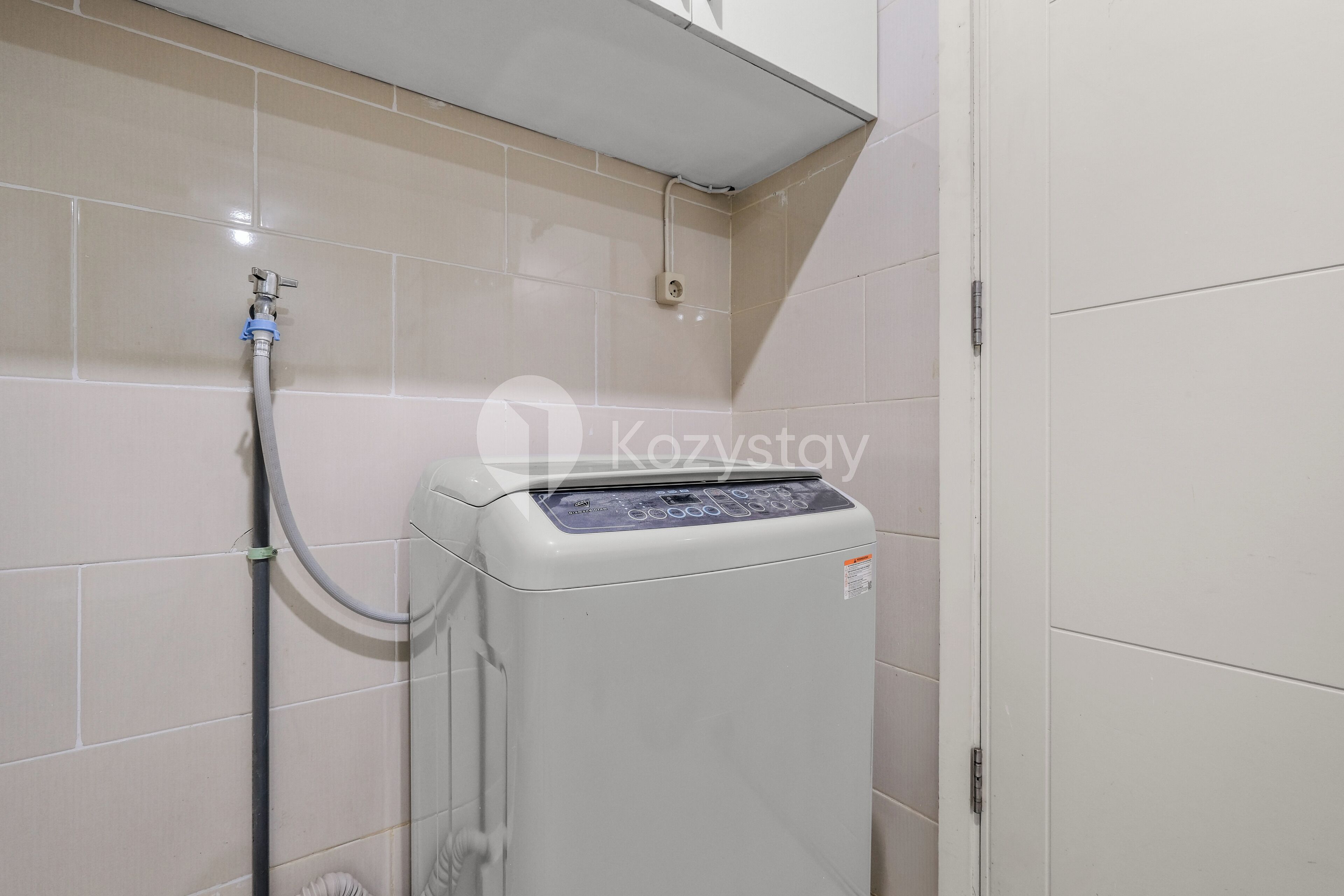 Un lavadero pequeño y moderno con lavadora y secadora integradas, una manguera para agua y un panel de control.