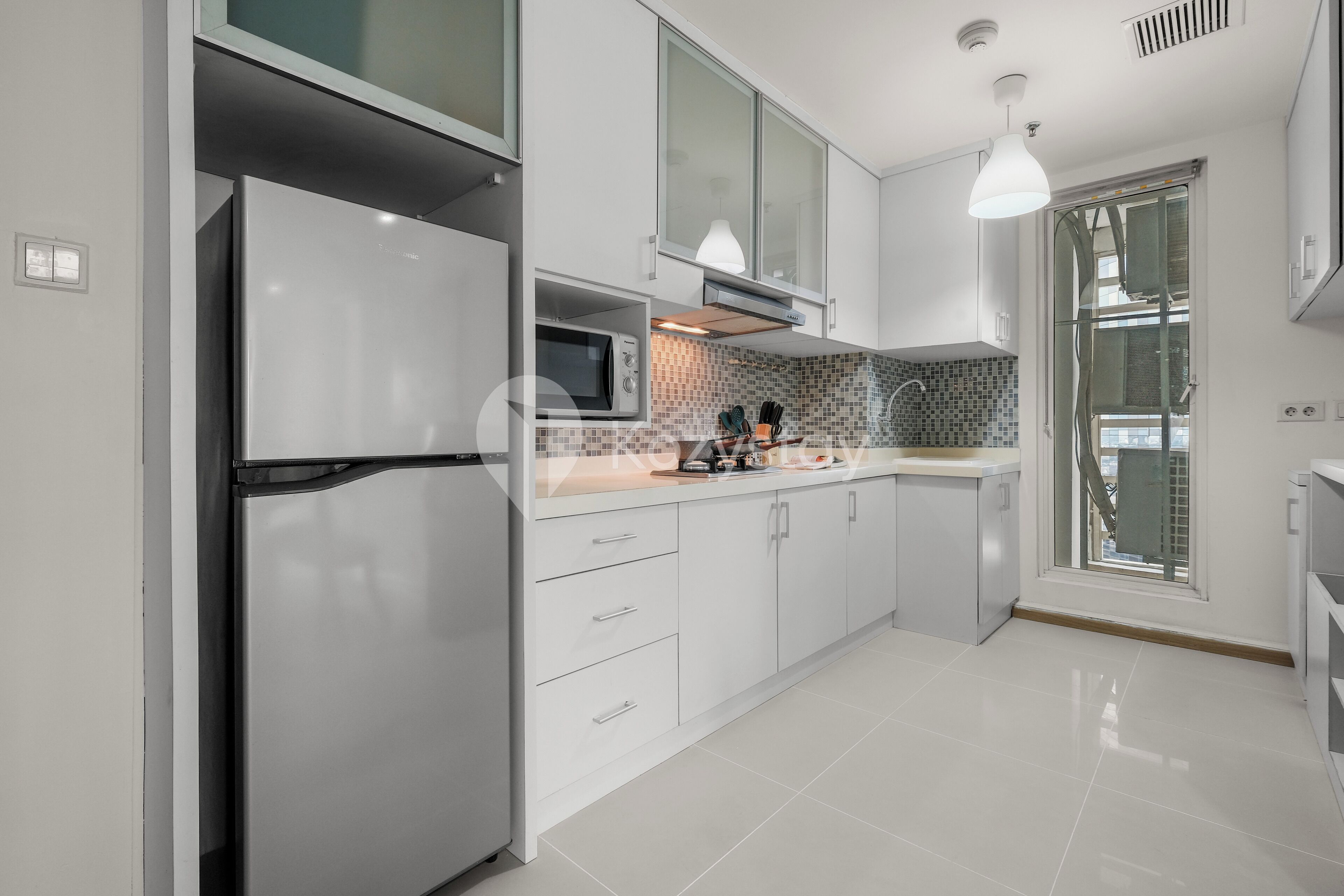 A modern kitchen with white cabinetry, a stainless steel refrigerator, a microwave, and a tiled backsplash.