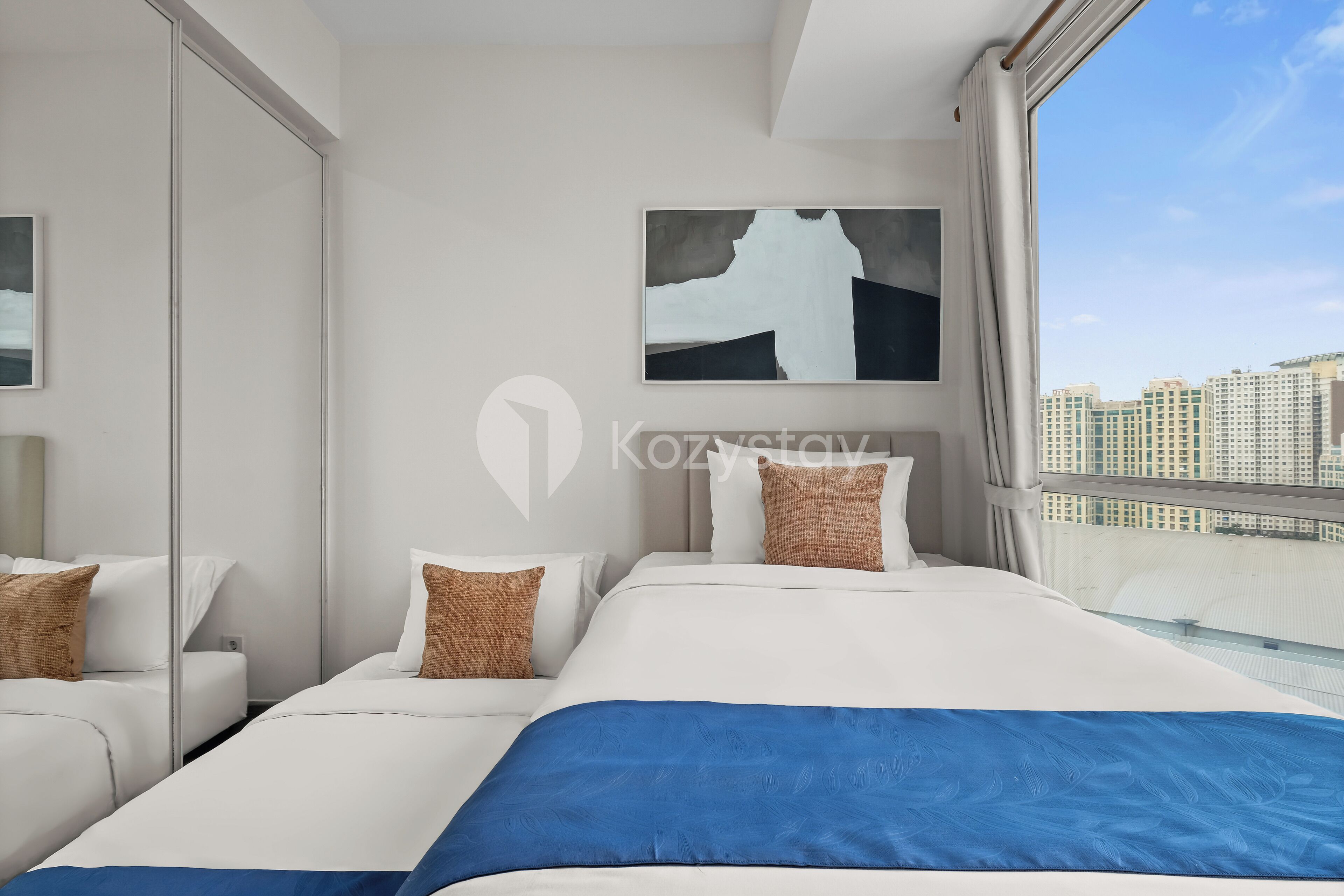 A modern hotel room with a large bed, a city view, and a painting on the wall.