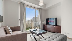 A modern living room with a sofa, ottoman, glass coffee table, and a TV on a wooden cabinet. - Serenya by Kozystay - Kuningan (Jakarta)