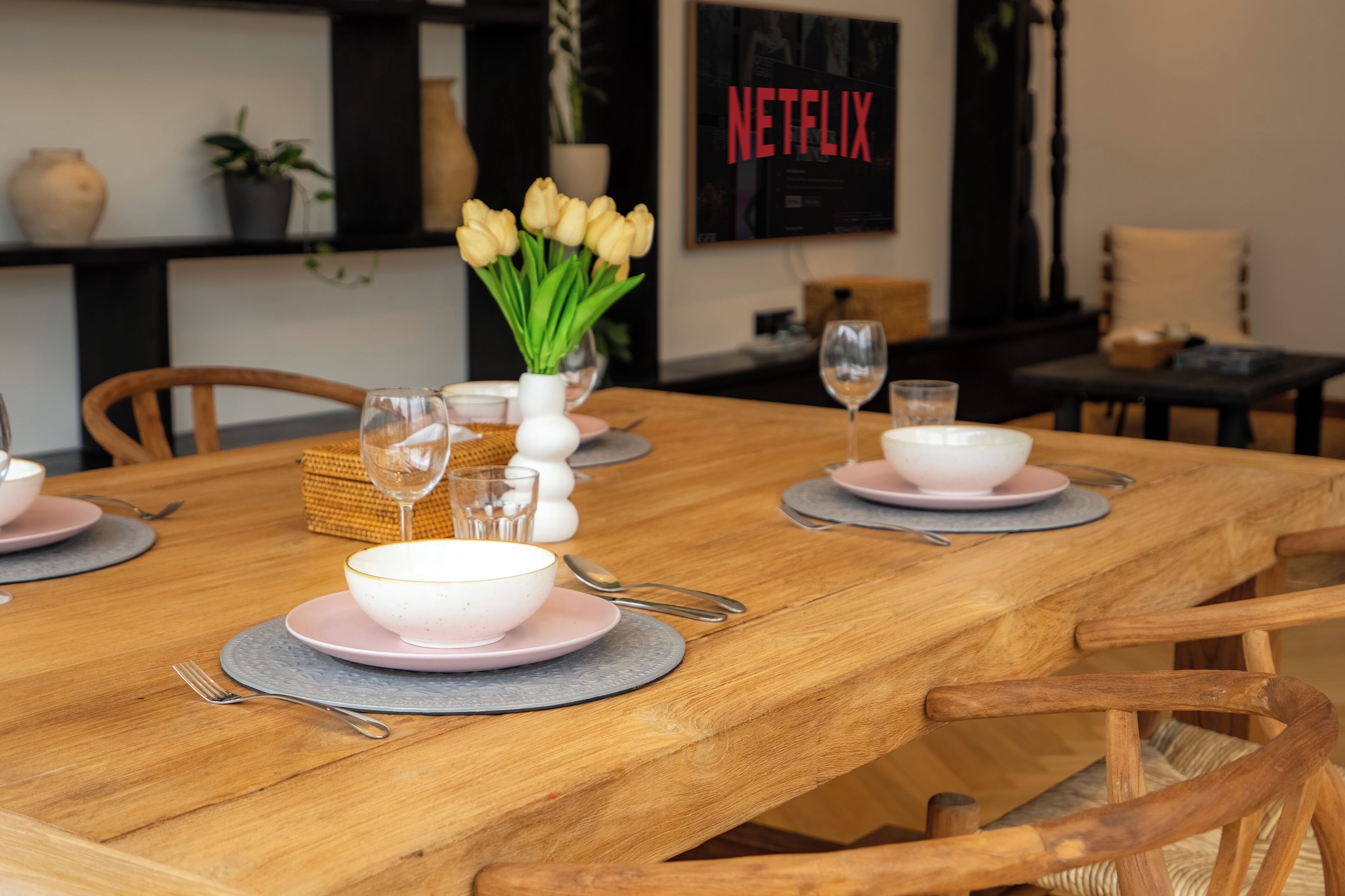 A dining table set with pink plates, bowls, and cutlery, surrounded by wooden chairs.
