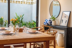A dining area with a wooden table set for four, surrounded by wicker chairs. A large mirror and a framed picture adorn the wall. - Black Villa by Betterplace (Tabanan)
