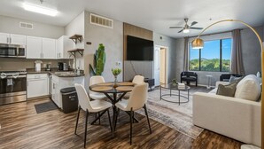 A modern apartment with a kitchen, dining area, and living room. It includes a flat-screen TV, ceiling fan, and large windows with a view. - Scottsdale 2BR/2BA • Pool • Gym • Free Parking (Phoenix)
