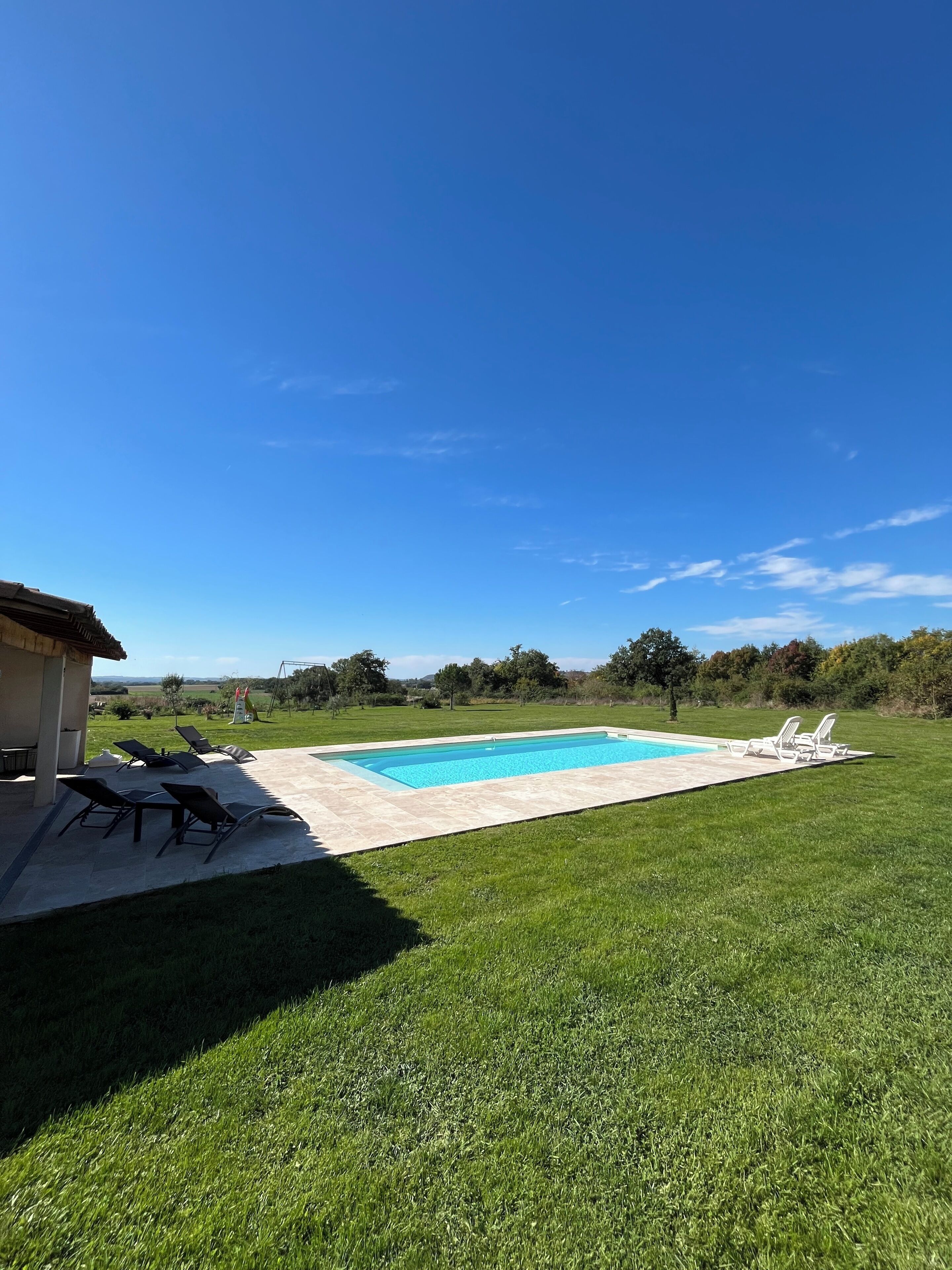 Une piscine avec des chaises longues, un patio couvert et une pelouse.