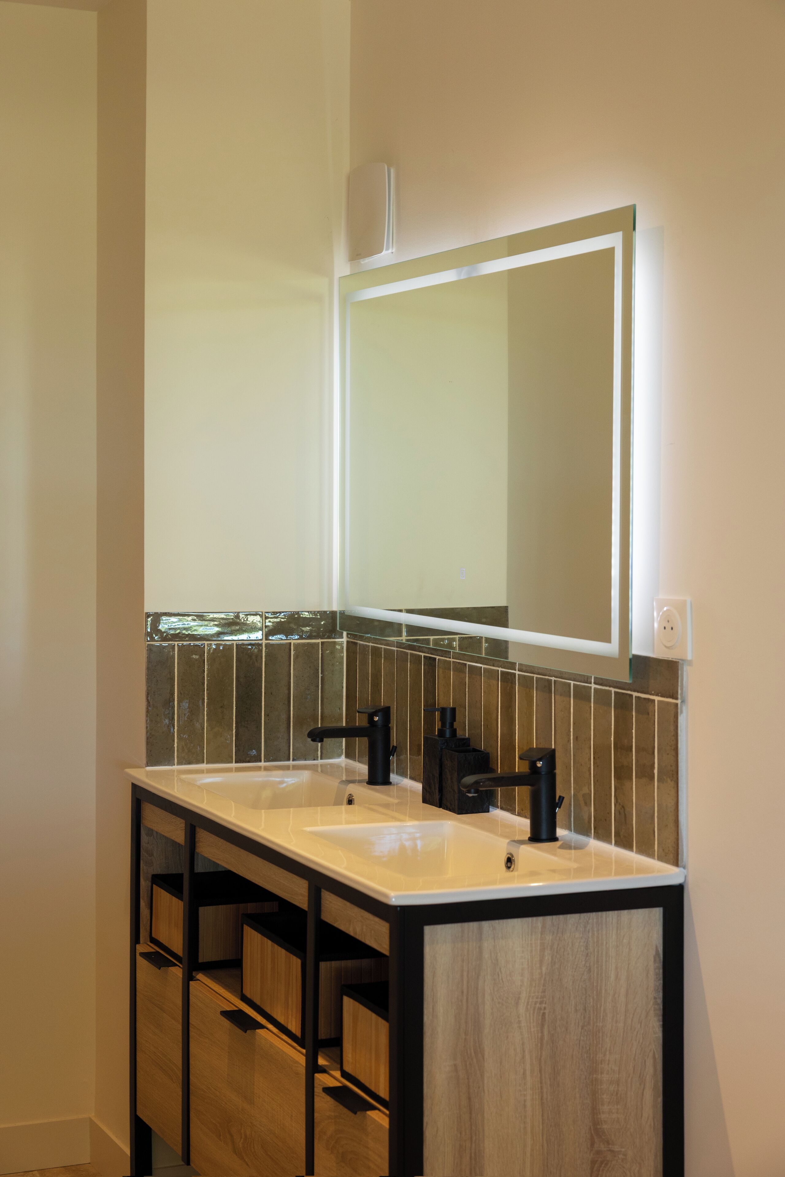 Ein Badezimmer mit zwei Waschbecken, einem Spiegel und einer gefliesten Rückwand.