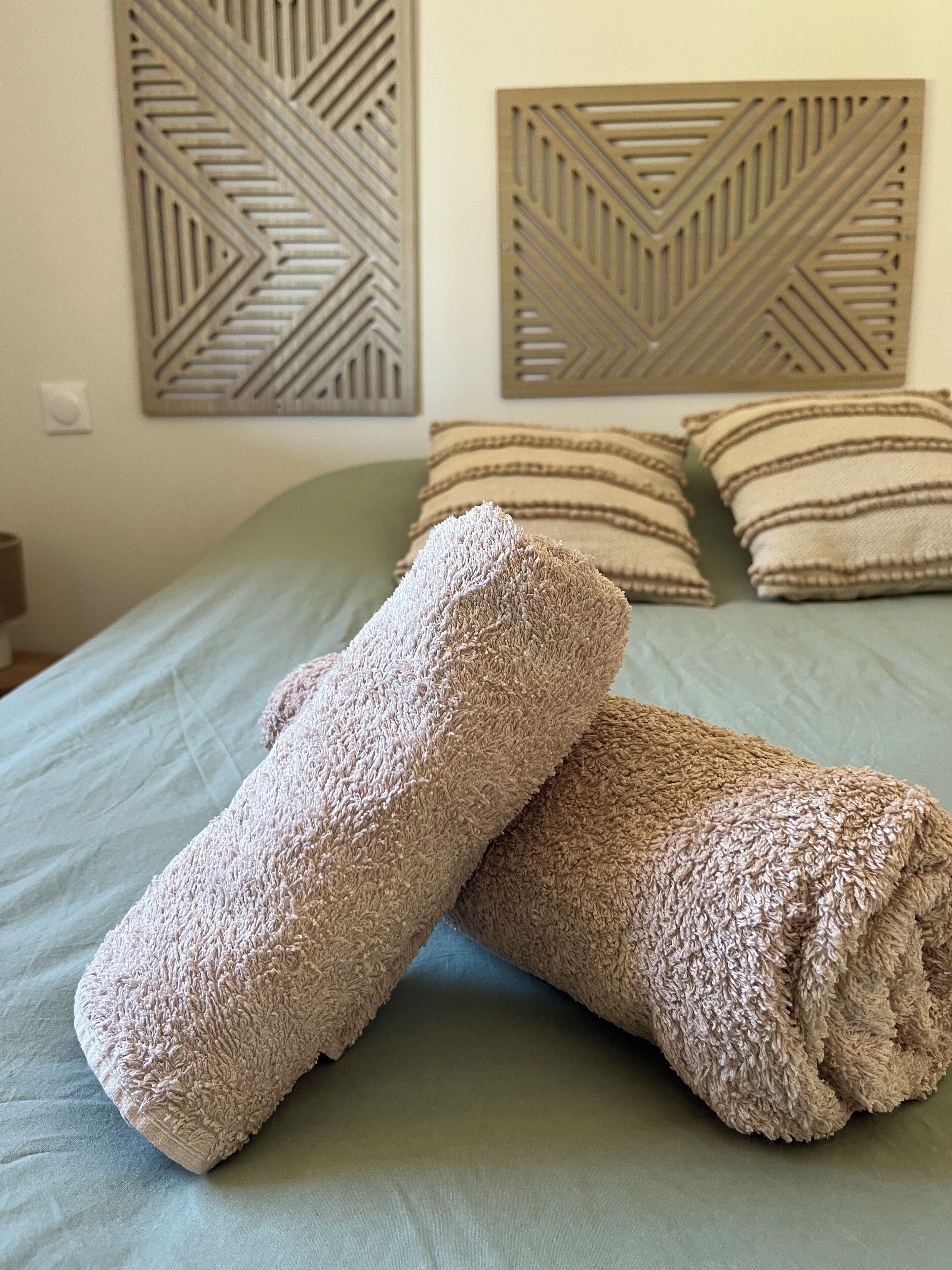 A bed with two rolled towels and two pillows on a green bedspread.