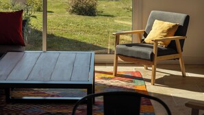 A room with a large sliding glass door leading to a garden. Inside, there is a wooden table and a chair with a cushion. - Renovated farmhouse with swimming pool, pétanque and country views (Coufouleux)