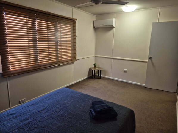 Ein Schlafzimmer mit einem Bett, einem kleinen Tisch mit Pflanze, einem Kleiderschrank und einer Klimaanlage.