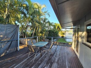 Eine Holzterrasse mit Tisch und Stühlen, umgeben von Palmen und Blick auf einen Pool.