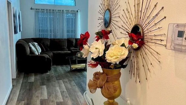 A living room with a dark-colored sofa, a decorative wall mirror, and a vase with flowers.