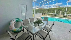 A glass-top table with six chairs, a pool in the background, and a covered patio area.
