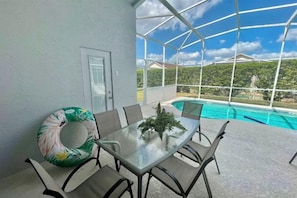 Une terrasse extérieure avec une table en verre, des chaises et une piscine en arrière-plan.
