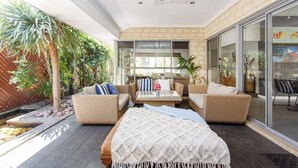 Un espacio exterior moderno con mobiliario de mimbre, una mesa de vidrio y vistas al jardín.