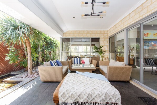 Un espace de vie extérieur moderne, aménagé avec des meubles en osier, une table en verre et offrant une vue sur le jardin.