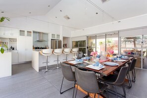 Une cuisine moderne avec des meubles blancs, un îlot central doté de tabourets de bar et un coin repas avec une grande table dressée pour six personnes.