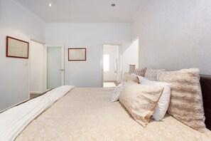 Une chambre avec un grand lit, deux portes et un miroir au mur.