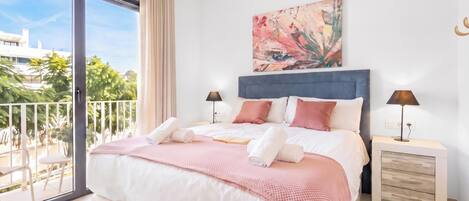 Un dormitorio moderno con una cama grande, dos mesitas de noche, vistas al exterior y un cuadro en la pared.