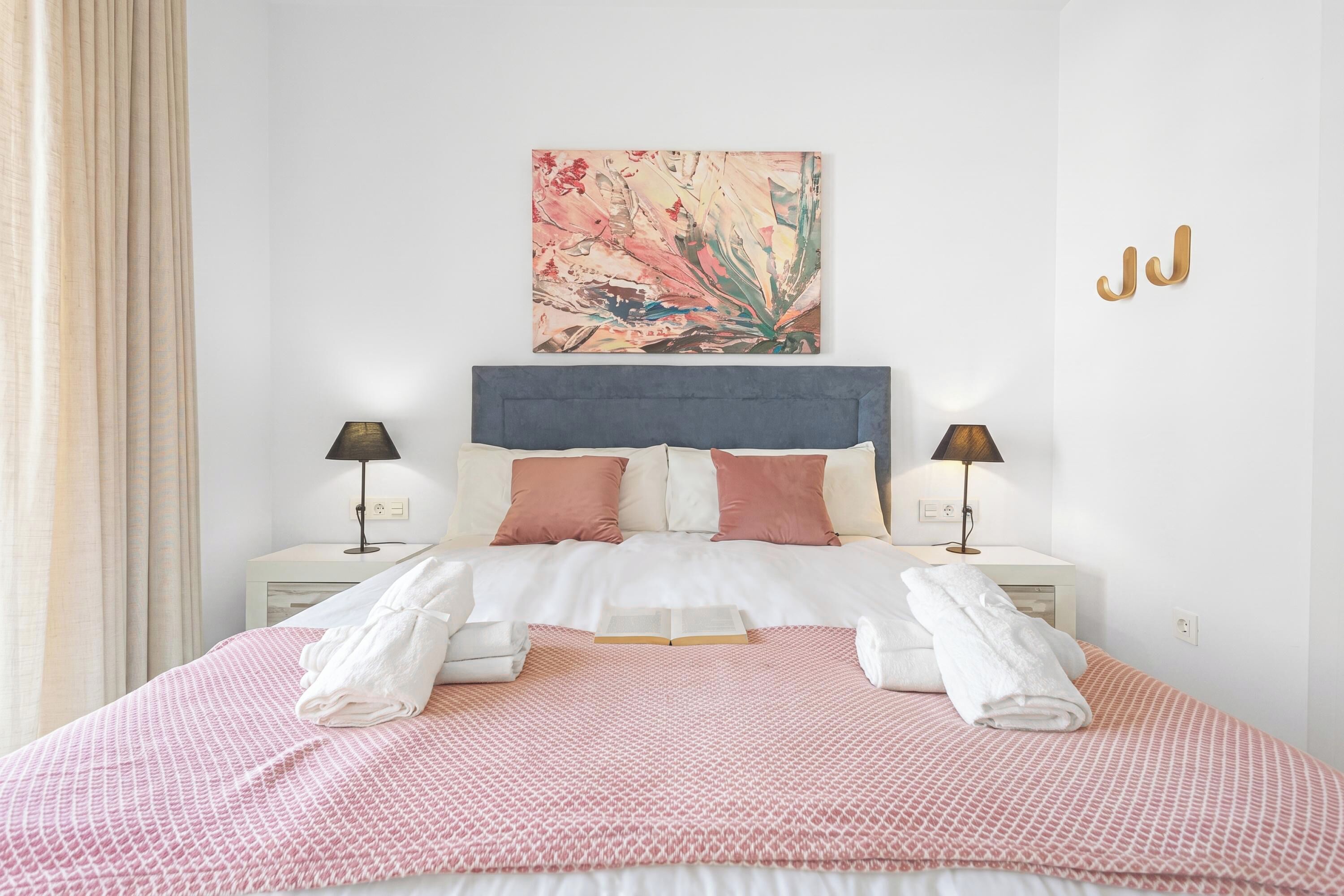 Una camera d'albergo con un letto, due comodini, un quadro e una lampada a parete.