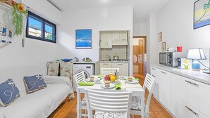 Een kleine leefruimte met een eethoek, kitchenette en een slaapbank.
