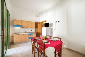 A dining area with a red tablecloth, wooden chairs, and a kitchen in the background. - Borgo Primizia T3 Pool and Sea, Otranto, Italy (Otranto)