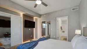 Una moderna camera d'albergo con un letto grande, una ventola a soffitto, una televisione a schermo piatto montata a parete e un bagno visibile attraverso una porta aperta.
