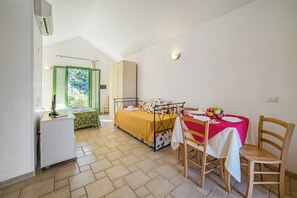 A bedroom with a bed, bedside table, and a small desk with a chair. There is a window with curtains, a wardrobe, and a table with chairs. - Borgo Primizia M16 Pool And Sea, Otranto, Italy (Otranto)