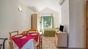 Una zona de menjador amb una taula preparada per a dues persones, un llit amb un estovat verd i un escriptori amb un ordinador.