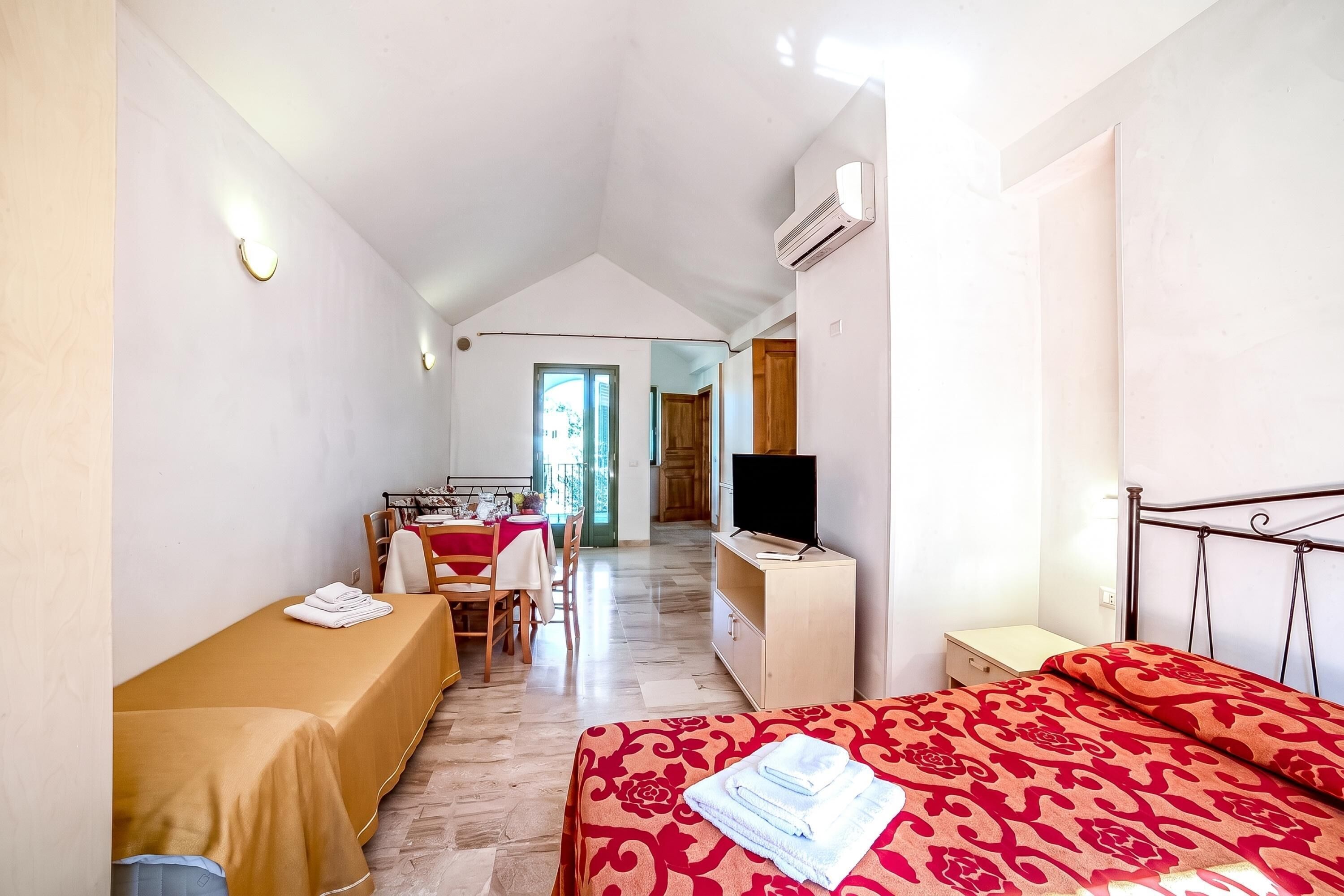 A hotel room with a bed, a TV, a desk, and a chair. There is a window and a door leading to another room.