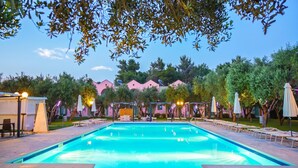 Ein Schwimmbecken mit Liegestühlen und Sonnenschirmen, umgeben von Bäumen und einem Gebäude mit rosafarbenen Wänden.