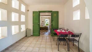 Ein Essbereich mit einem roten Tisch und schwarzen Stühlen, einer grünen Tür, die in einen anderen Raum führt, und einem gefliesten Boden.
