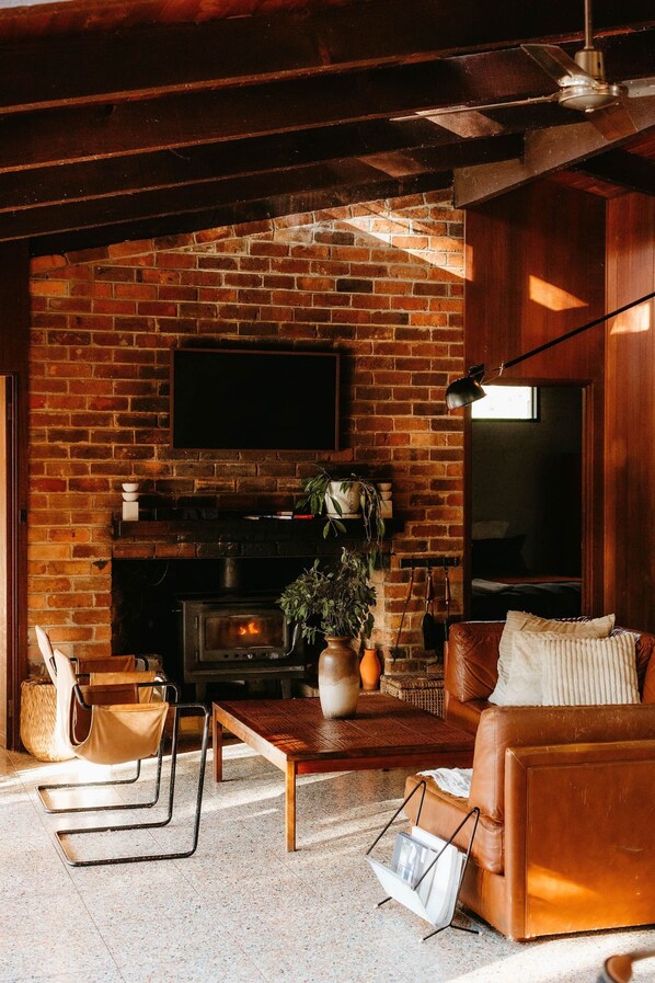 Una sala de estar acogedora con chimenea de ladrillo, sofá de cuero y televisor de pantalla plana en la pared.
