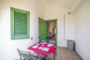 A dining area with a table set for two, green shutters, and a view into the kitchen.