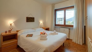 Une chambre d’hôtel avec un grand lit, deux tables de chevet, une fenêtre avec des rideaux, un radiateur et un tableau accroché au mur.