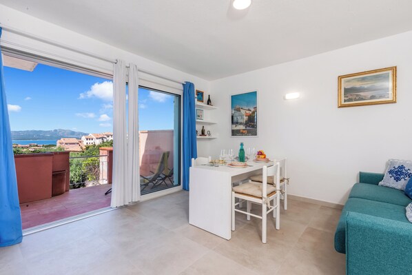 A room with a balcony, a dining area, a sofa, and a painting on the wall. - Aironi 34, Porto Rotondo, Italy (Porto Rotondo)