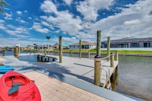 Un muelle frente al agua con kayaks, cielo despejado y un edificio al fondo.