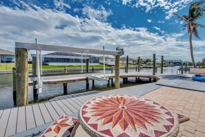 A waterfront area with a dock, a covered seating area, and a building in the background. - Golden Globe - luxury on the canal with pool/spa (Cape Coral)
