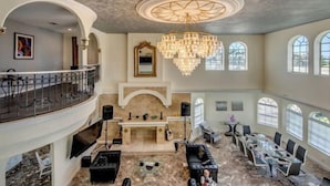 A spacious interior with a grand chandelier, a fireplace, and a balcony overlooking the area. - Golden Globe - luxury on the canal with pool/spa (Cape Coral)