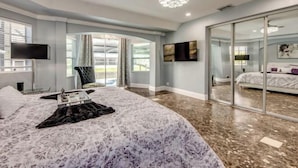A bedroom with a large bed, a TV, a chandelier, and a sliding glass door leading to a balcony. - Golden Globe - luxury on the canal with pool/spa (Cape Coral)