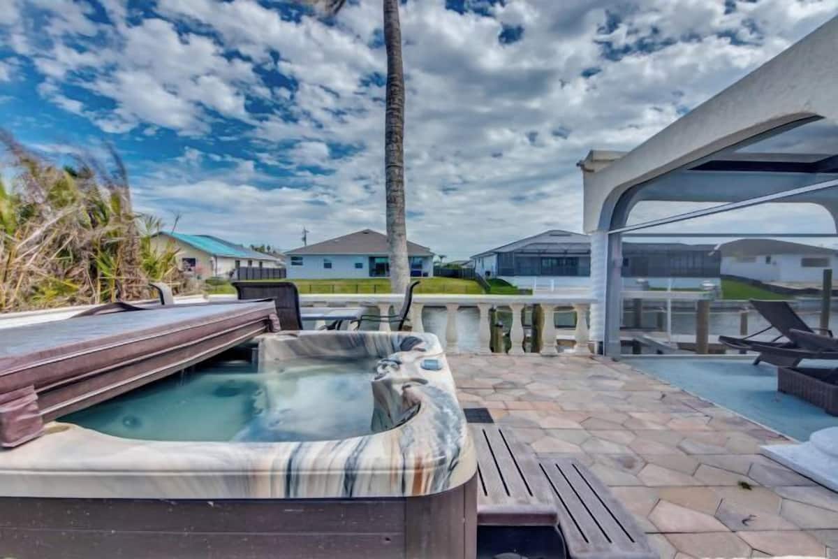 A hot tub with a stone exterior, outdoor seating, and a view of houses in the background.