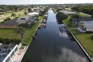 A canal with boats docked on the right, surrounded by residential buildings and greenery. - Golden Globe - luxury on the canal with pool/spa (Cape Coral)