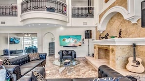 A spacious living area with a high ceiling, a fireplace, and a mounted television. - Golden Globe - luxury on the canal with pool/spa (Cape Coral)